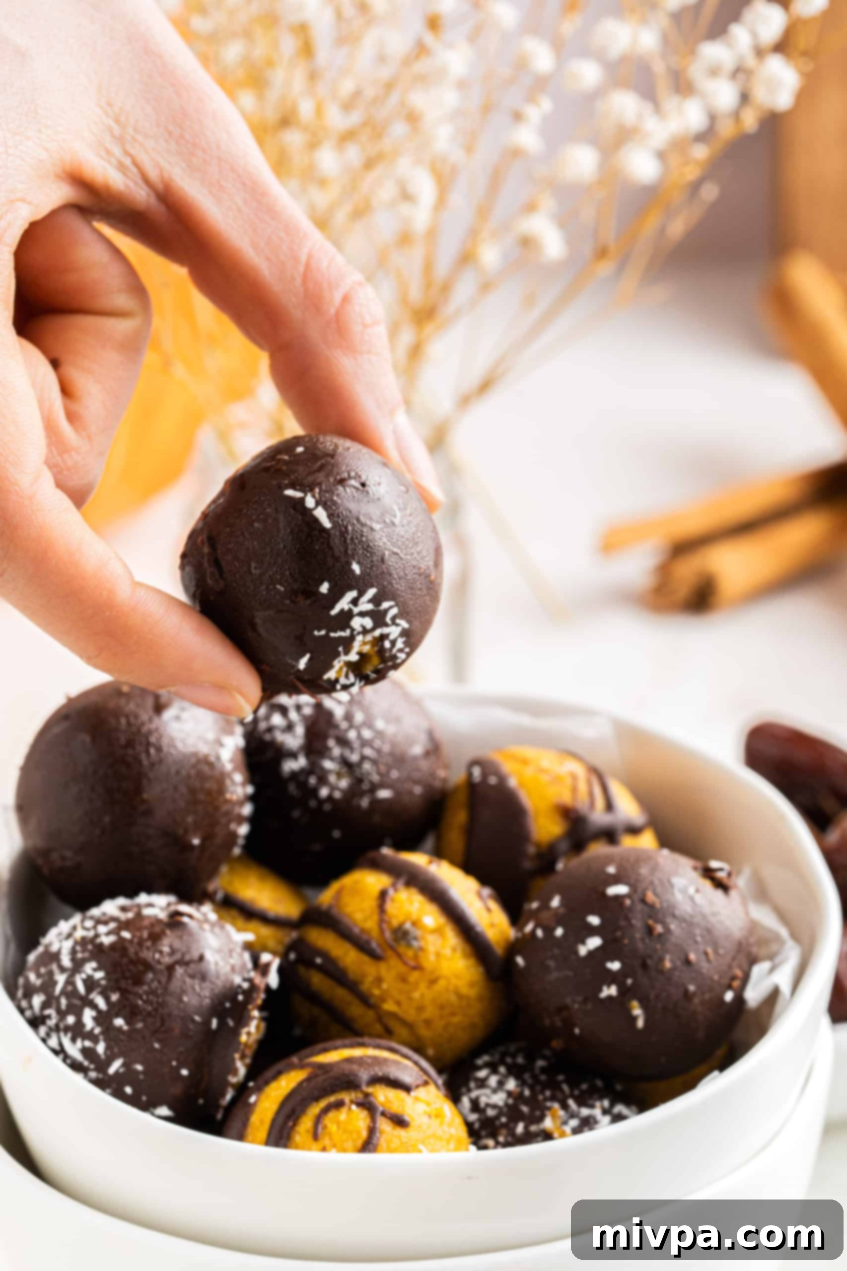 No-Bake Pumpkin Truffles (Gluten-Free, Vegan) A hand reaching for a delicious no-bake pumpkin pie truffle, coated in chocolate.
