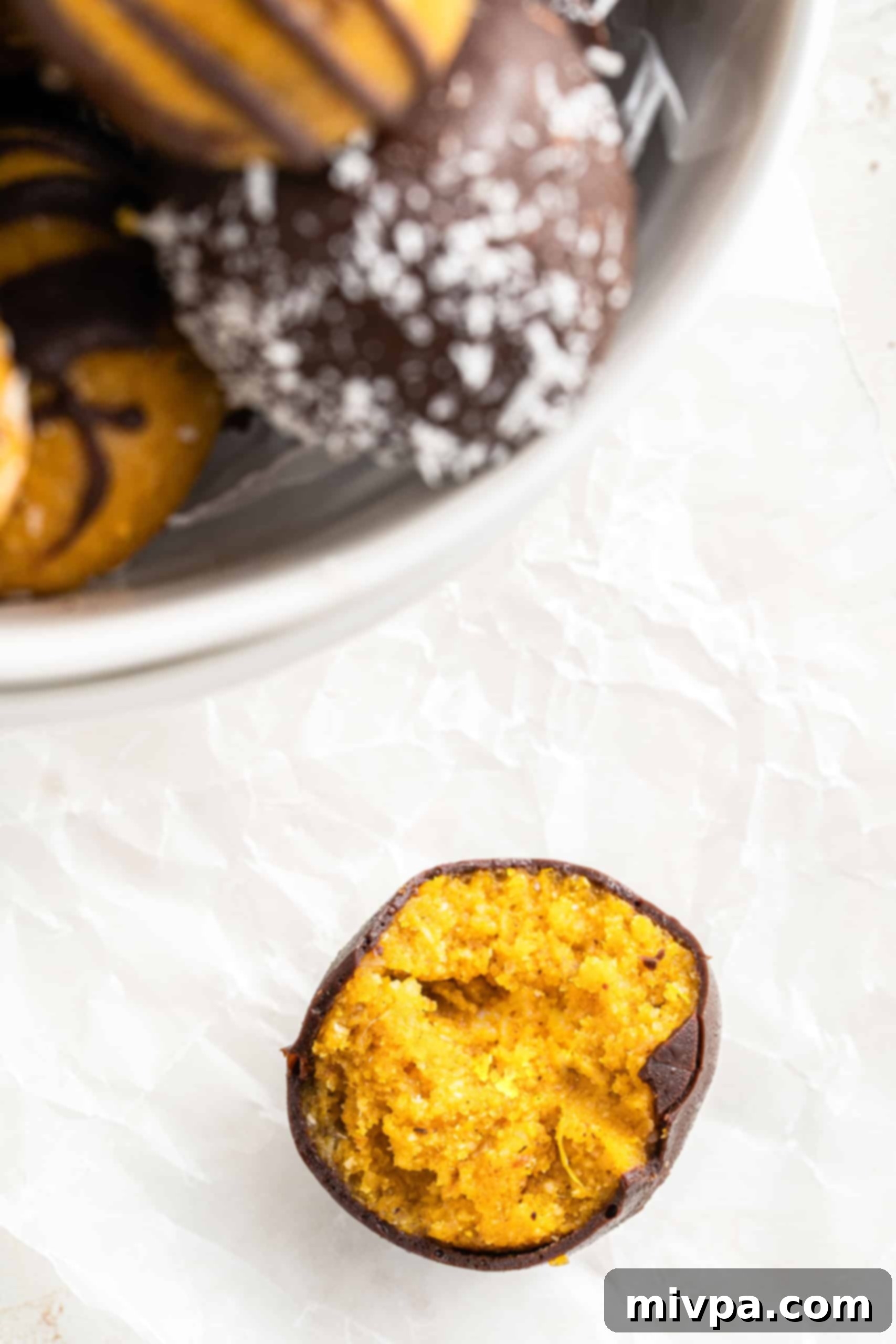 No-Bake Chocolate Pumpkin Spice Truffles (Gluten-Free, Vegan) An up-close shot of a half-eaten no-bake chocolate pumpkin truffle, revealing its creamy filling.