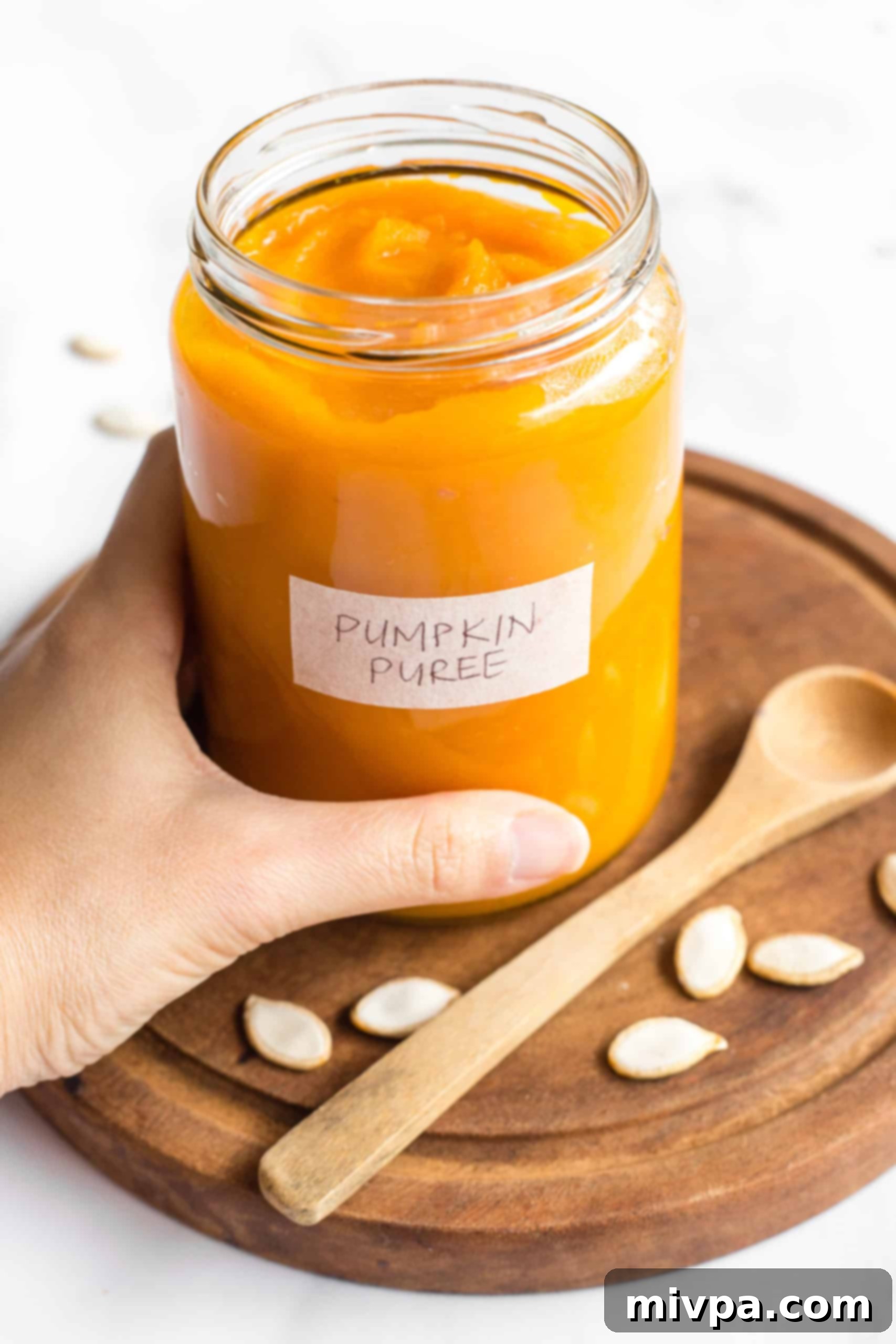 No-Bake Chocolate Pumpkin Truffles (Gluten-Free, Vegan) A hand gracefully holding a jar of rich, homemade pumpkin puree, perfect for these truffles.