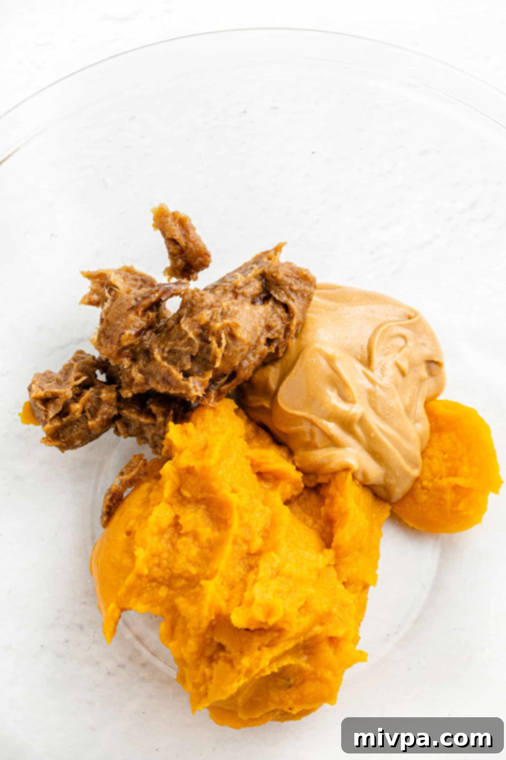 No-Bake Chocolate Pumpkin Balls (Gluten-Free, Vegan) A glass bowl containing the initial mixture of date paste, pumpkin puree, and almond butter, ready for the next ingredients.