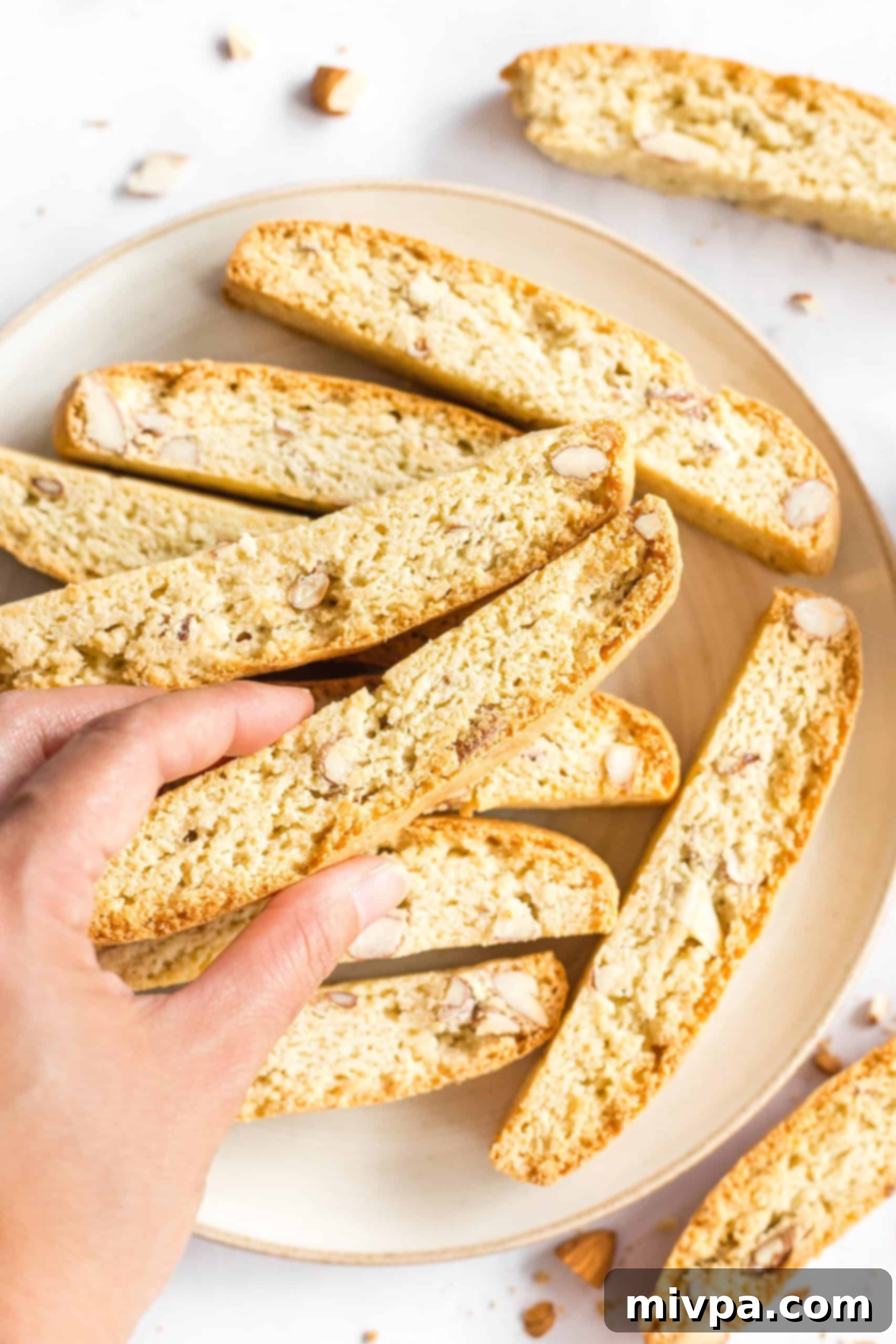 A hand gently holding a piece of perfectly baked, golden-brown gluten-free almond biscotti, ready to be enjoyed with a hot beverage.