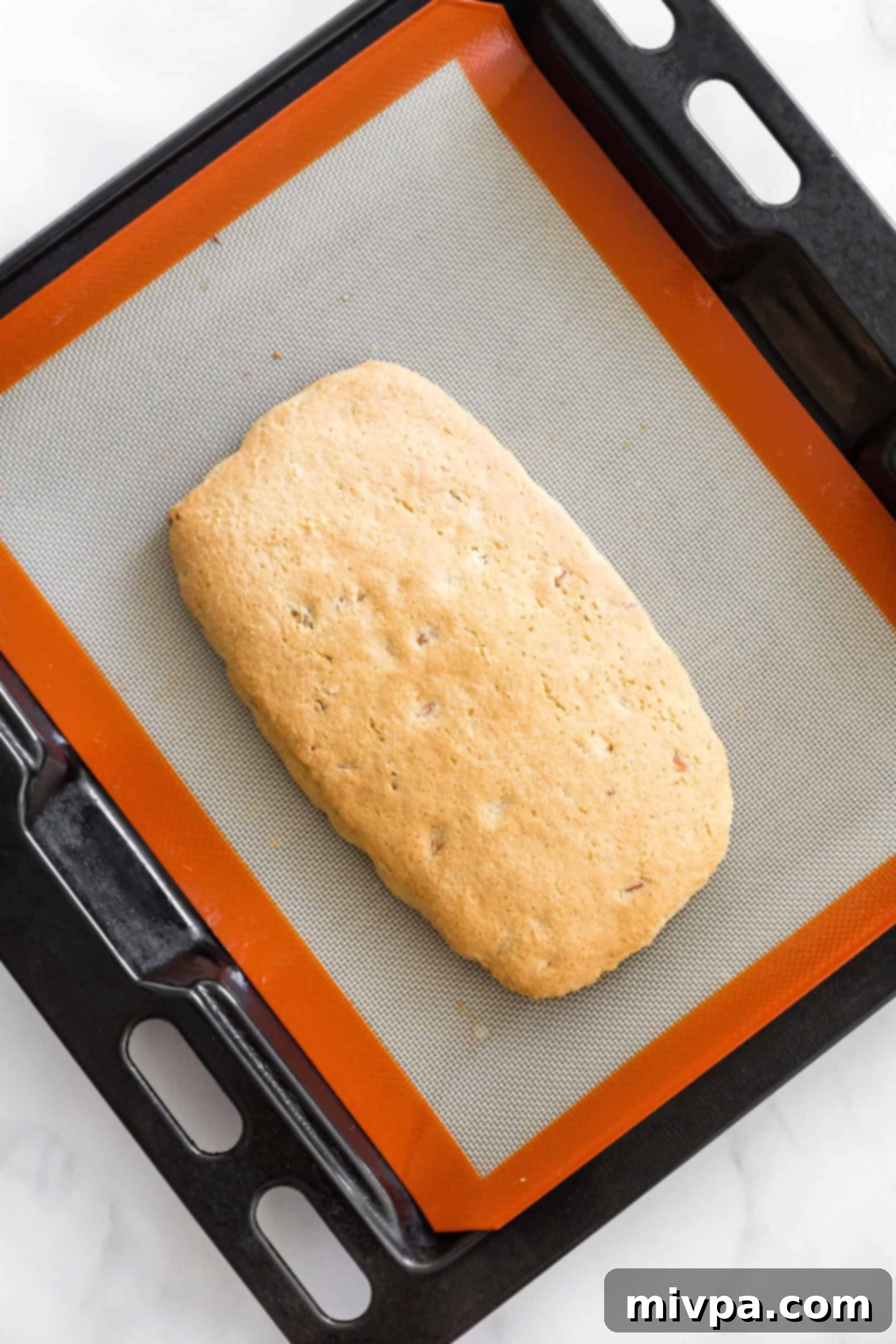 A freshly baked, golden-brown dough log resting on a silpat-lined baking sheet, cooling after its first bake.