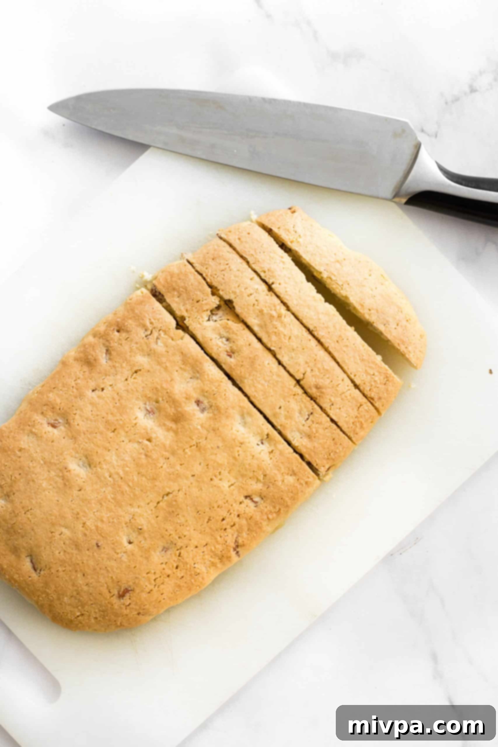 A baked dough log expertly sliced into uniform 1-inch pieces on a chopping board, ready for its second bake.