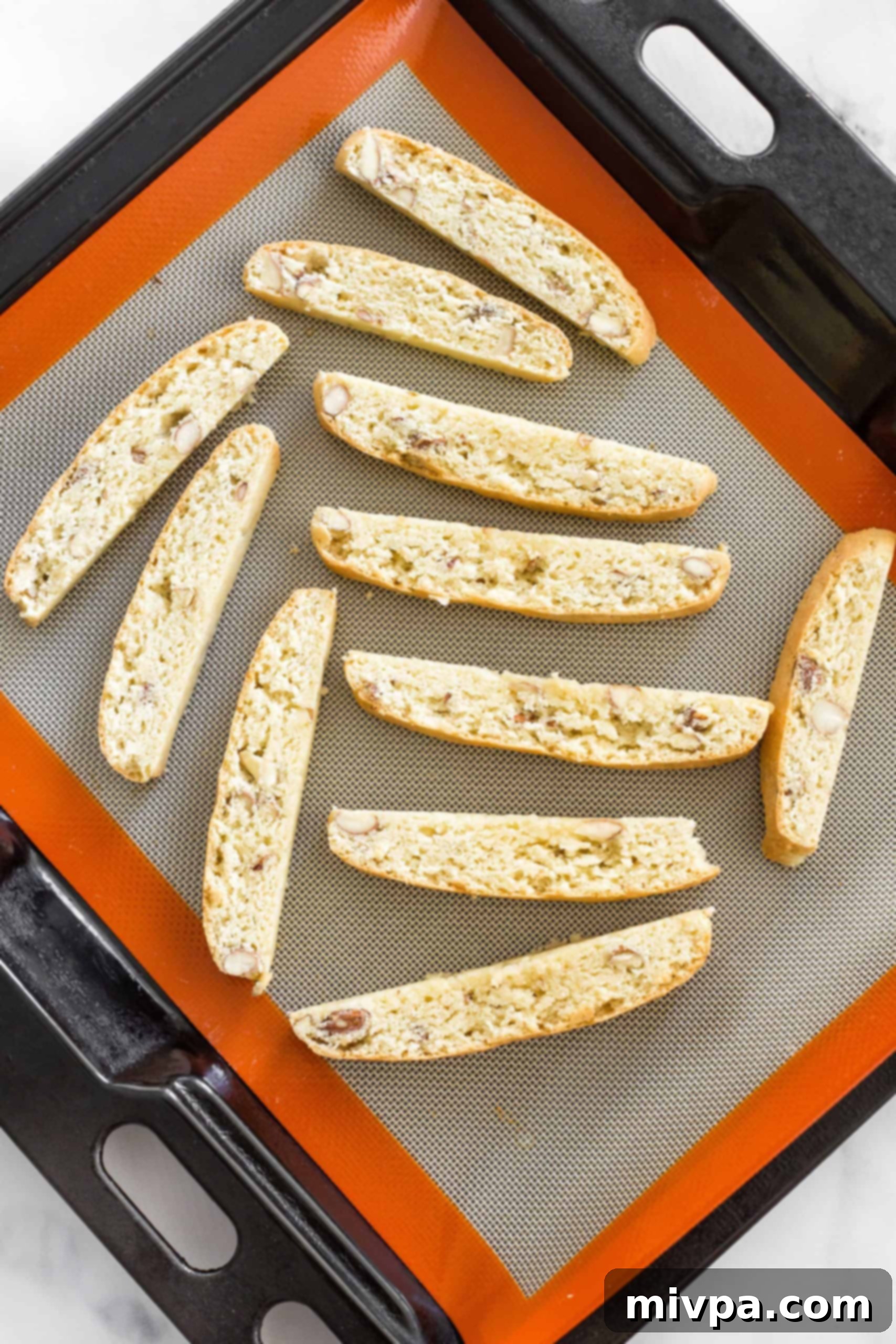 Rows of perfectly sliced biscotti arranged on a silpat-lined baking sheet, undergoing their second bake for ultimate crispness.