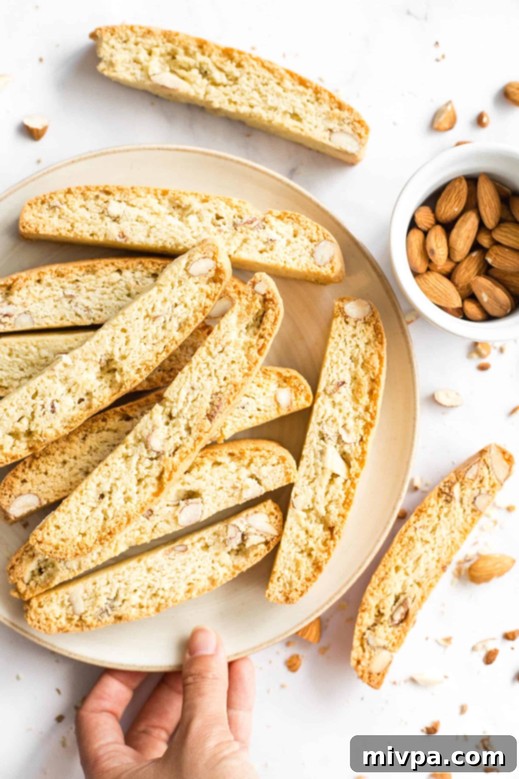 A beautifully arranged plate of gluten-free biscotti next to a pile of raw almonds, set against a classic marble background, highlighting the natural ingredients.