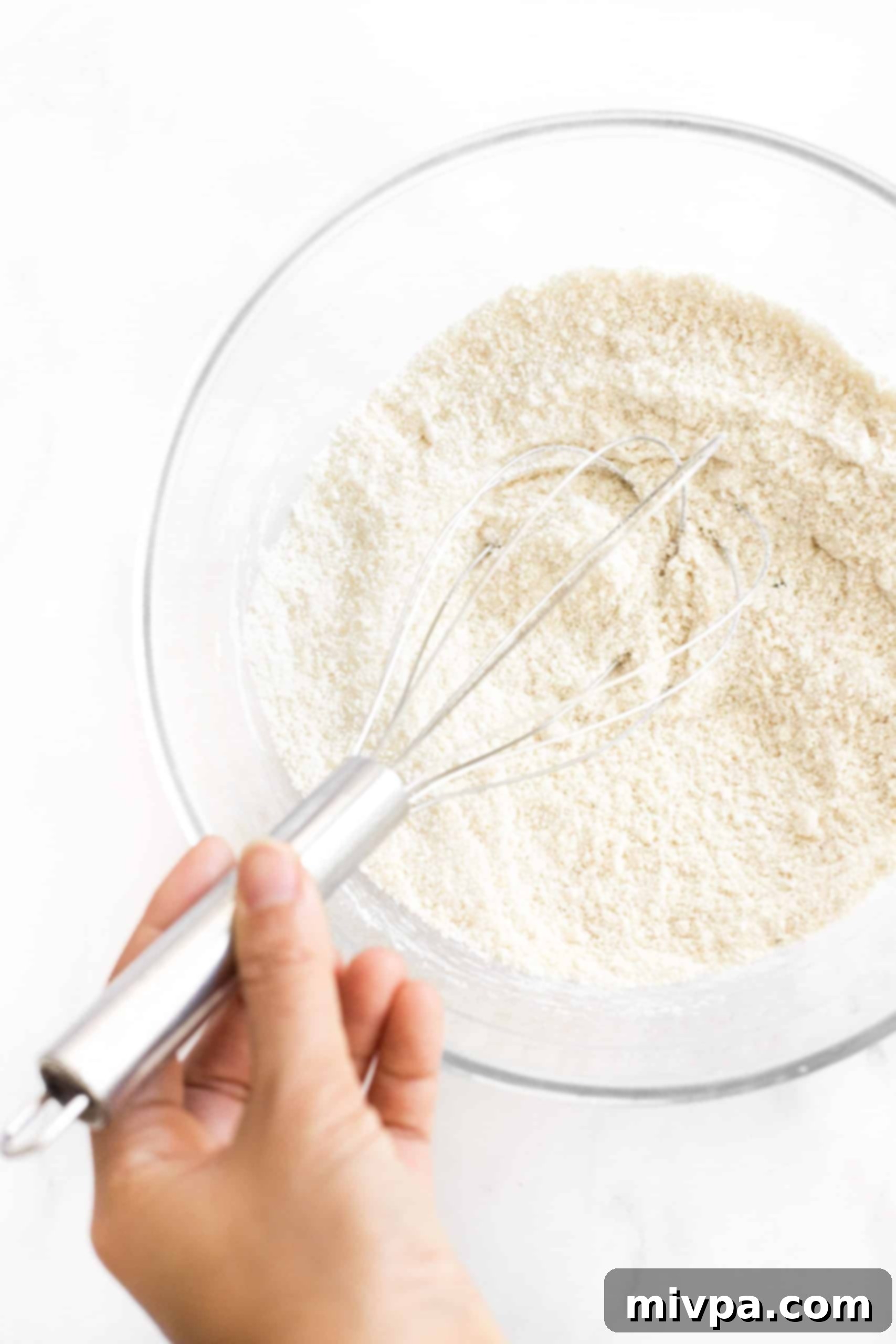 A glass mixing bowl with dry ingredients for biscotti, being whisked together to ensure an even blend.