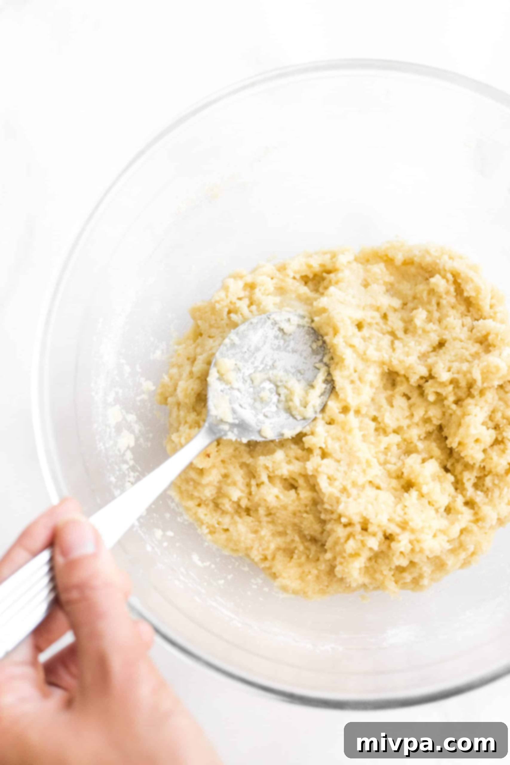 The process of mixing the wet and dry ingredients in a glass bowl to form a sticky, homogeneous biscotti dough.