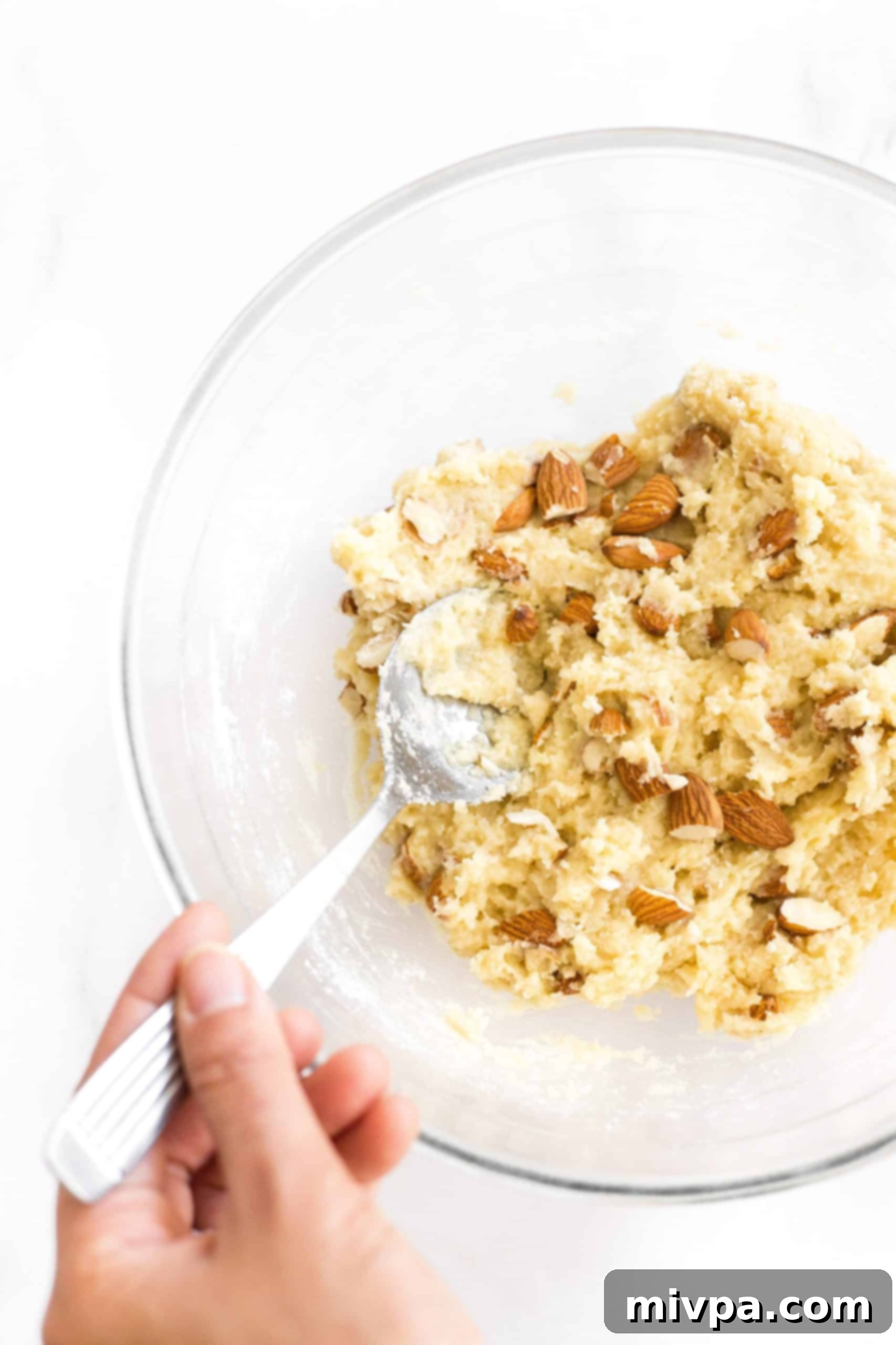 Chopped almonds being stirred into the prepared biscotti dough in a mixing bowl, ensuring even distribution.