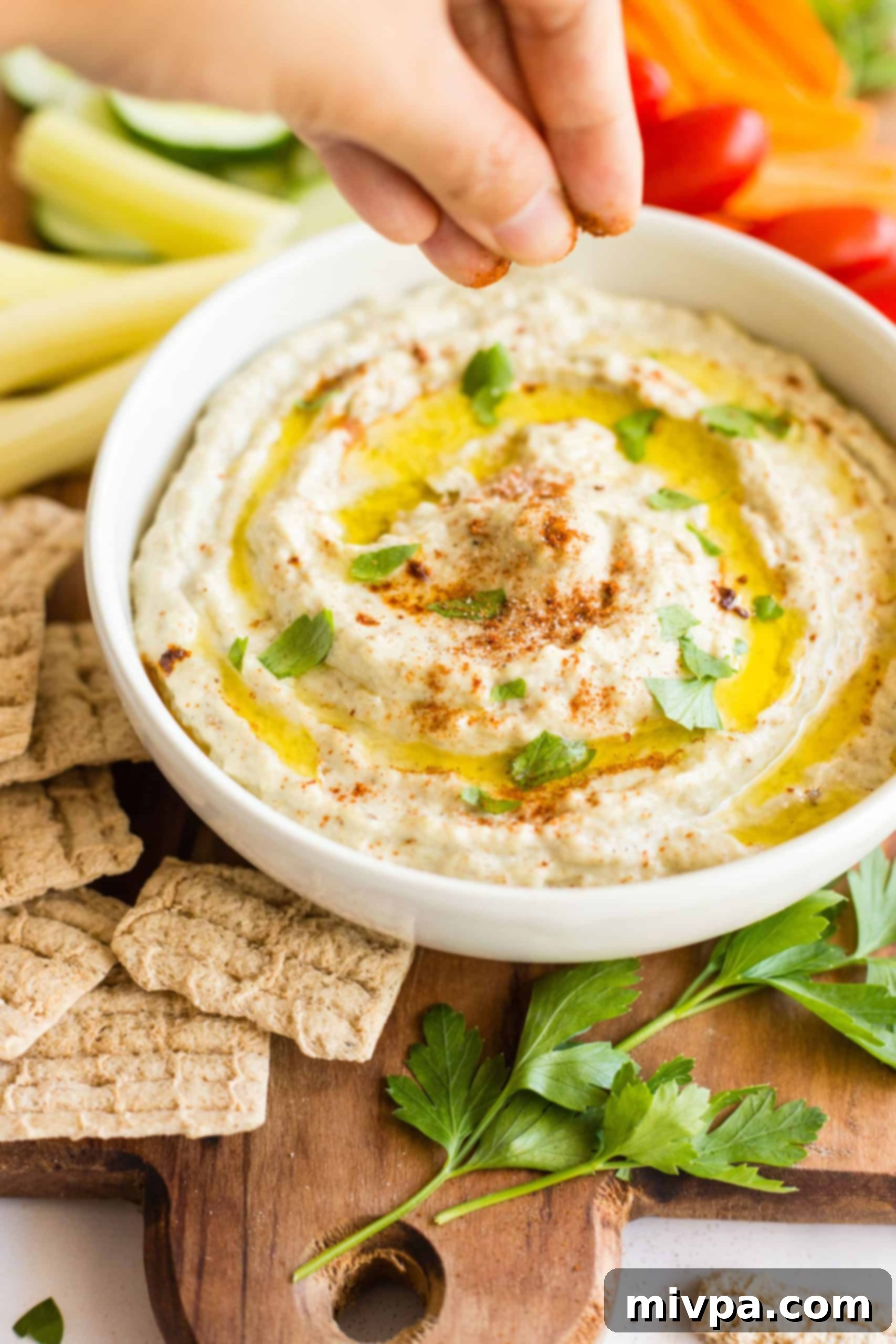 Hand sprinkling ground paprika over a bowl of baba ganoush.