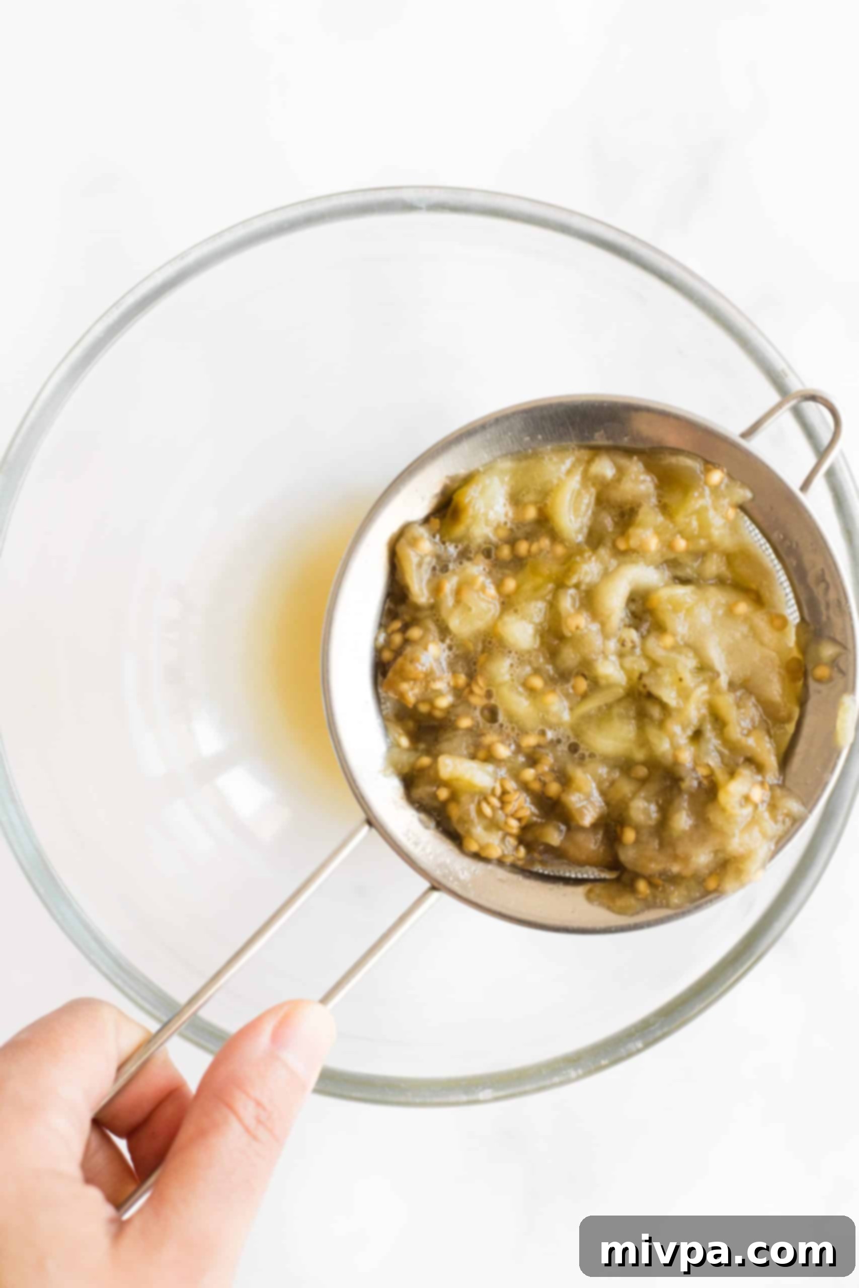 Straining the liquid from the eggplant flesh in a bowl.