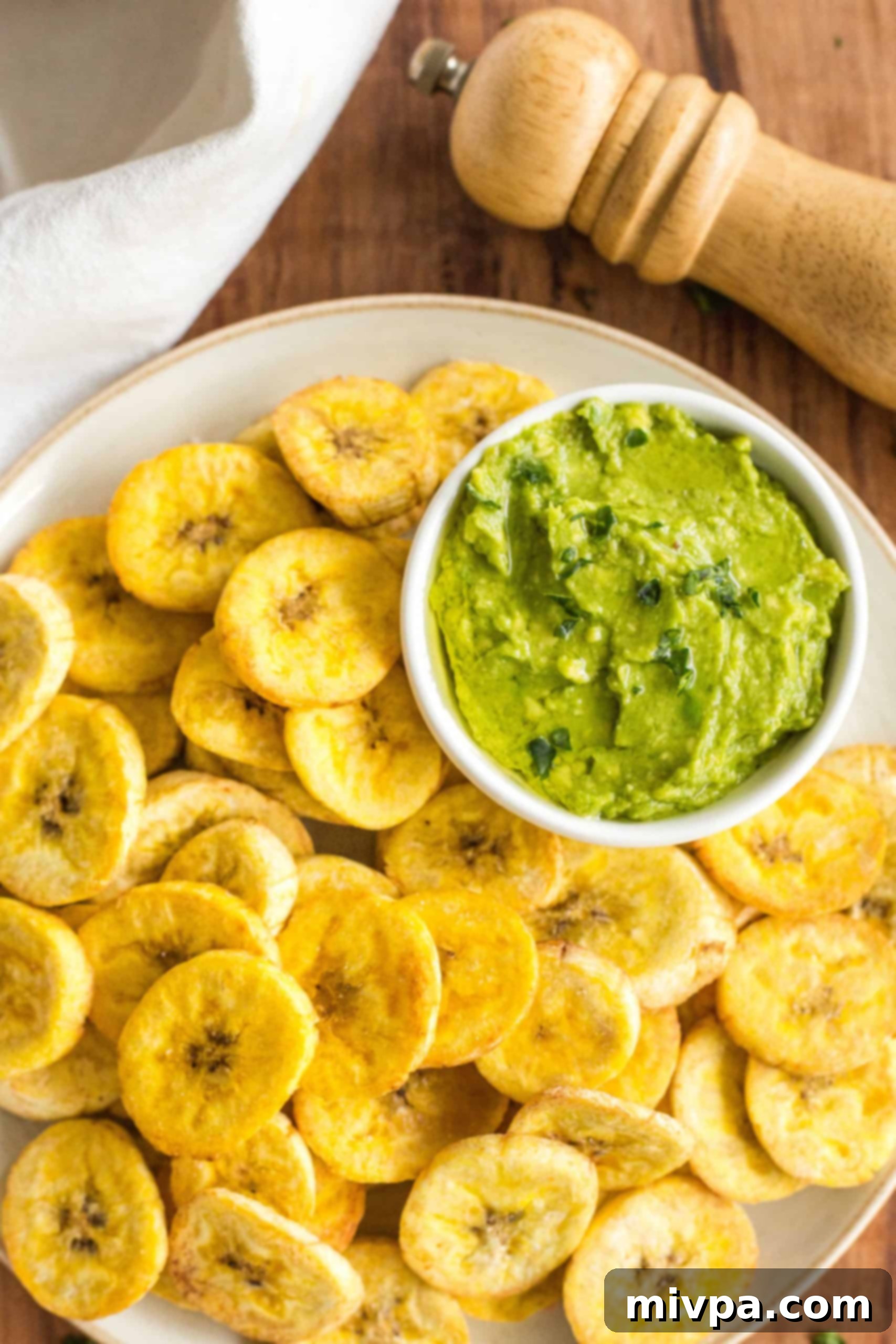 Air fryer plantains and a bowl of guacamole on a wooden board.