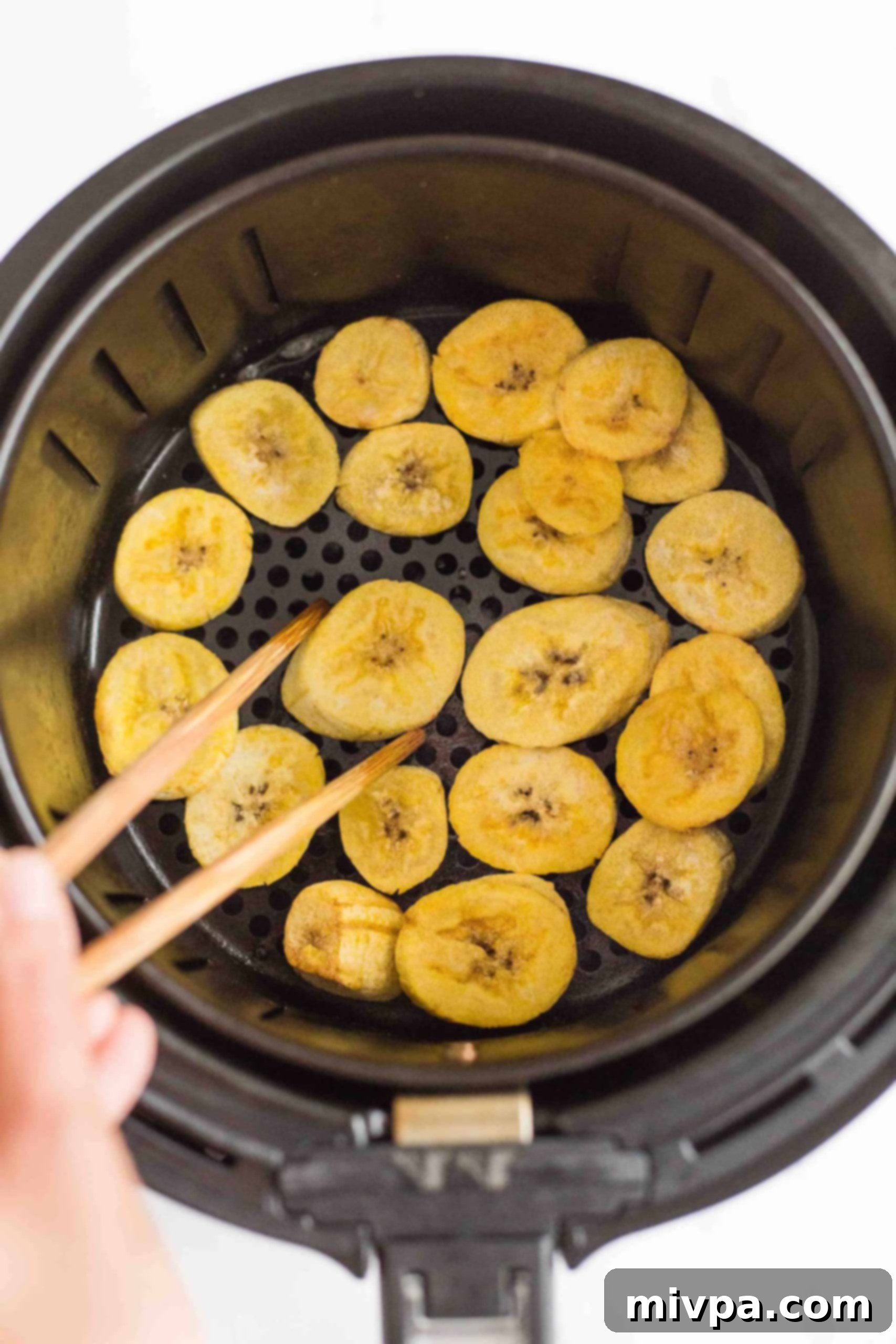Using chopsticks to flip over plantain slices in air fryer basket.