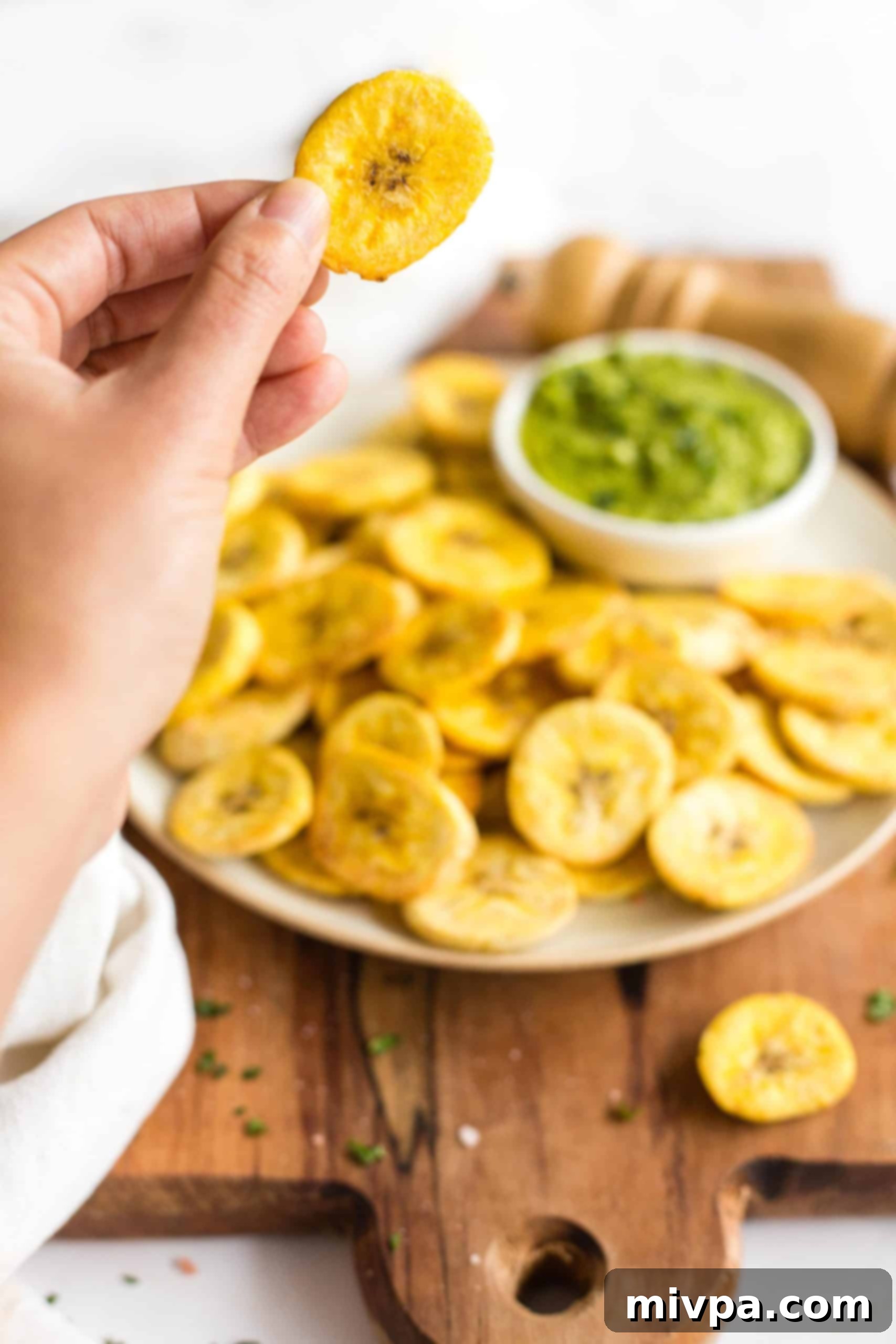 Hand holding up a crispy plantain chip.