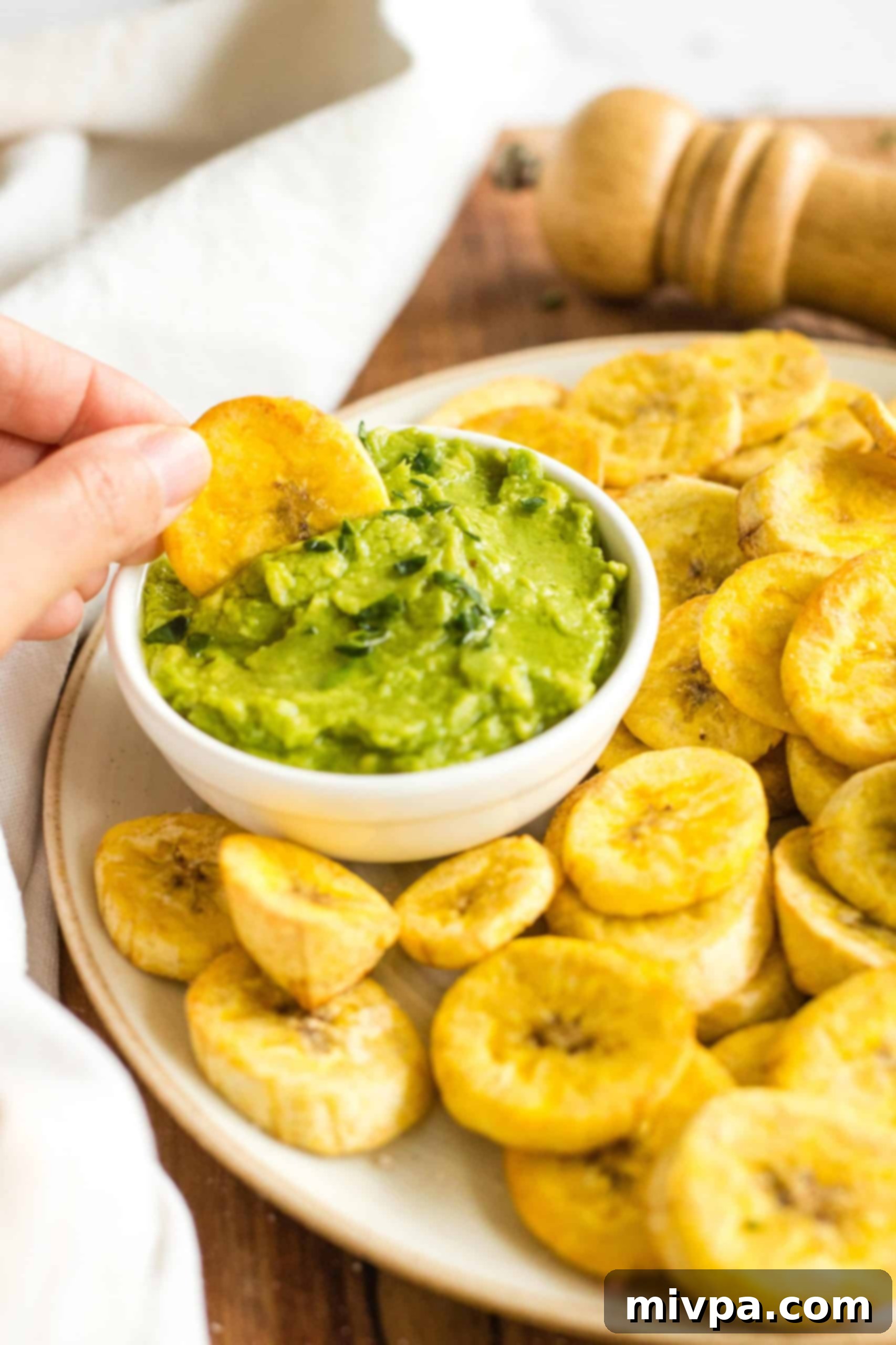 Dipping an air fryer plantain chip into a bowl of guacamole.