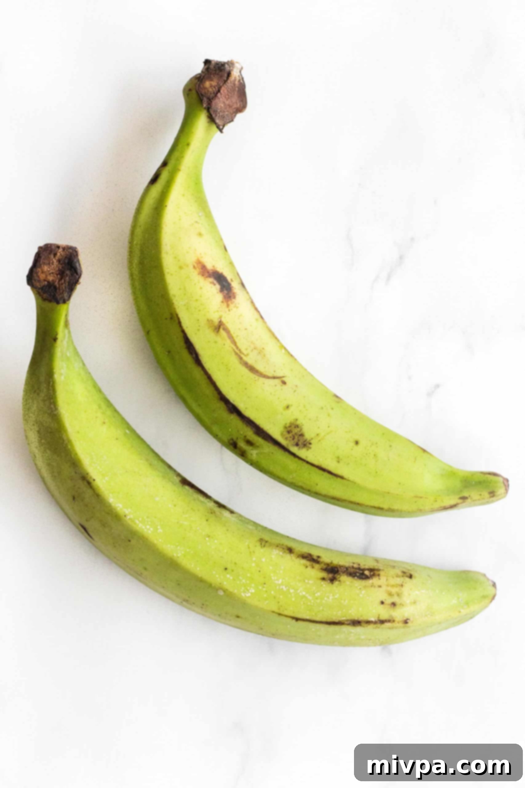 Green unripened plantains on a marble board.