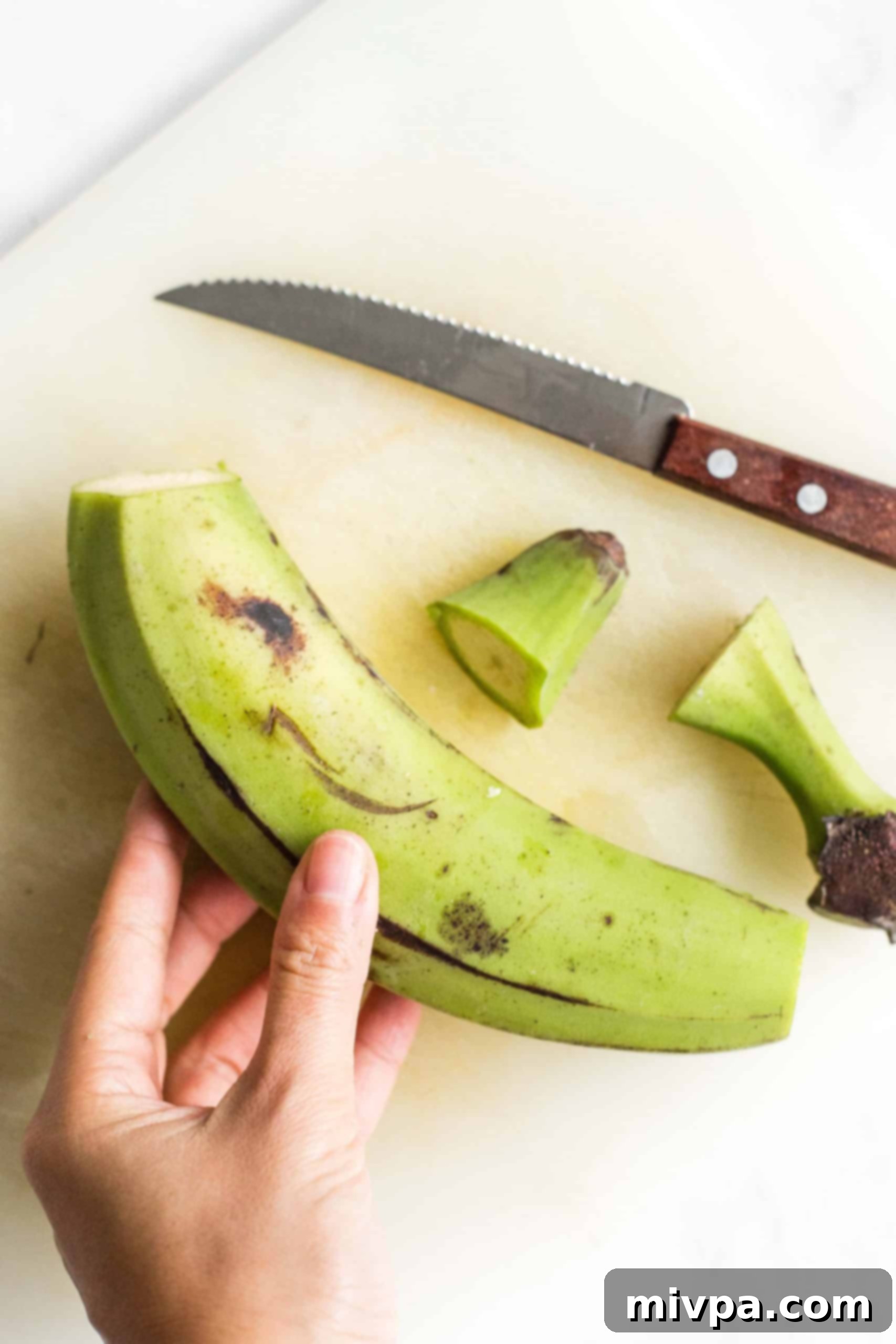 Holding a green plantain with its ends cut off.