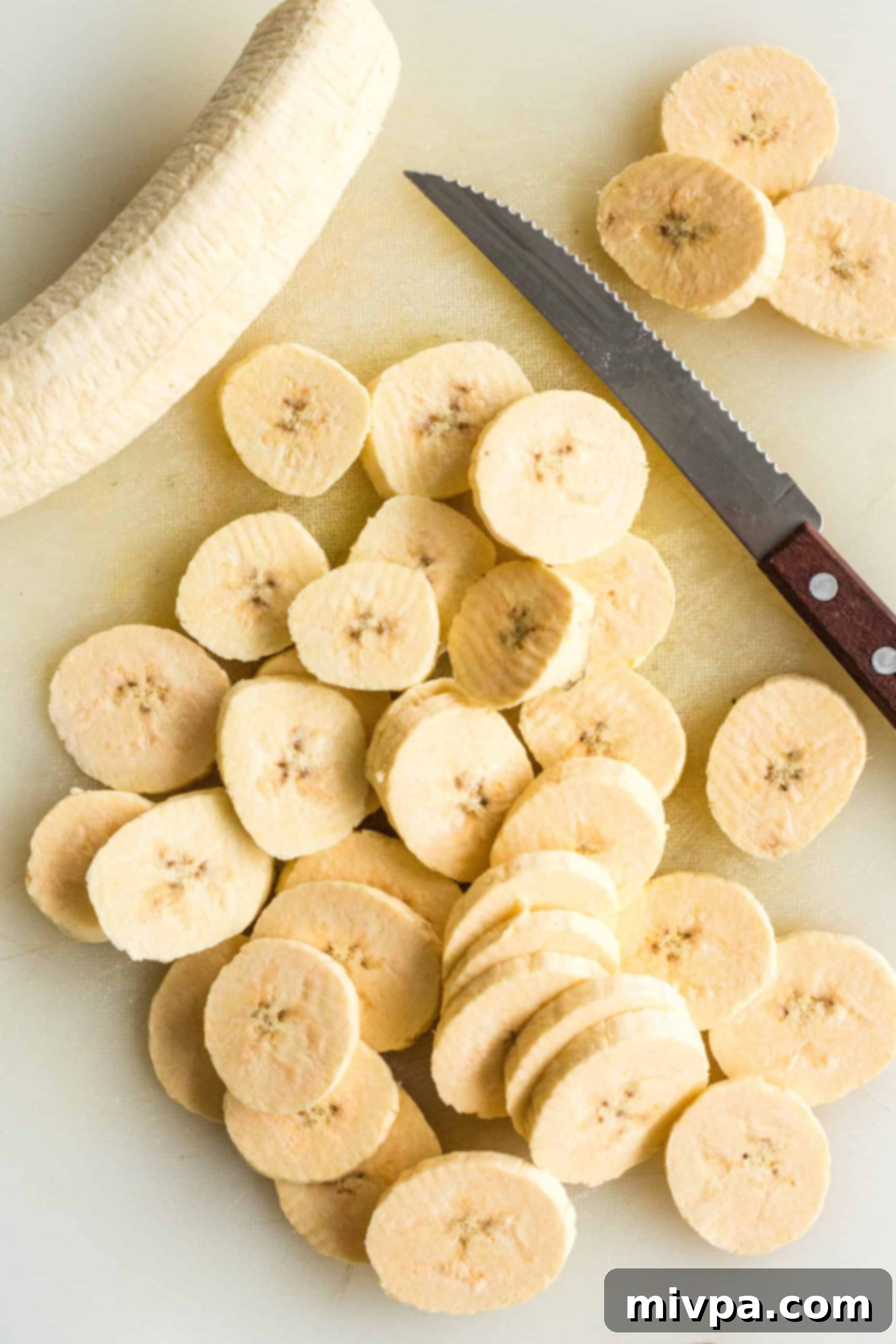 Sliced plantains and a knife on a chopping board.