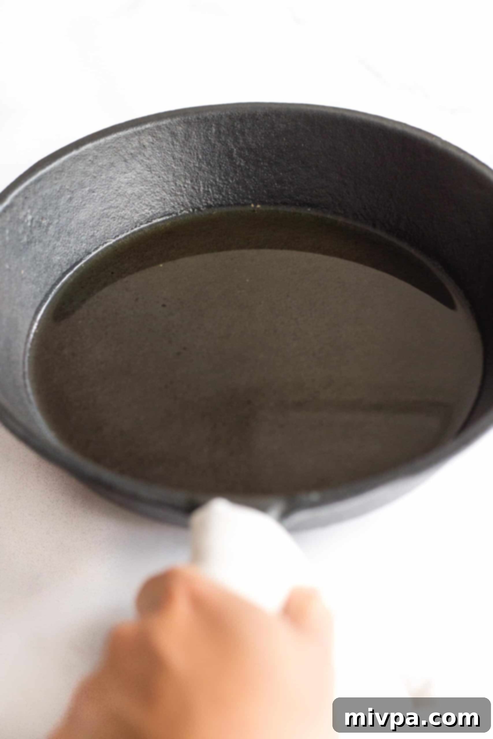 Easy Farinata Recipe - Chickpea Flatbread (Gluten-Free, Vegan) Carefully pouring olive oil into a hot cast iron skillet, held by an oven-mitted hand.