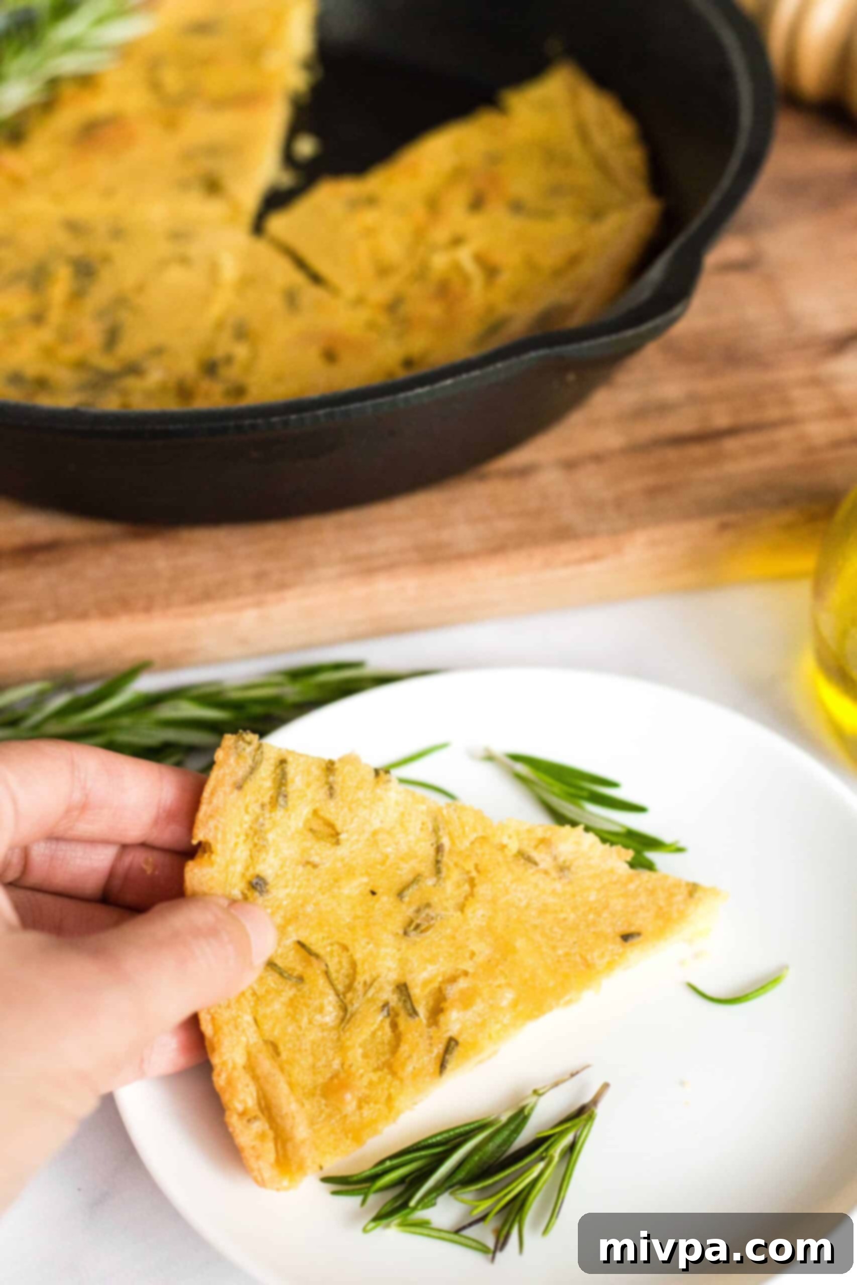 Easy Farinata Recipe - Chickpea Flatbread (Gluten-Free, Vegan) A hand holding a perfectly baked wedge of chickpea flatbread, showing its golden-brown crust.