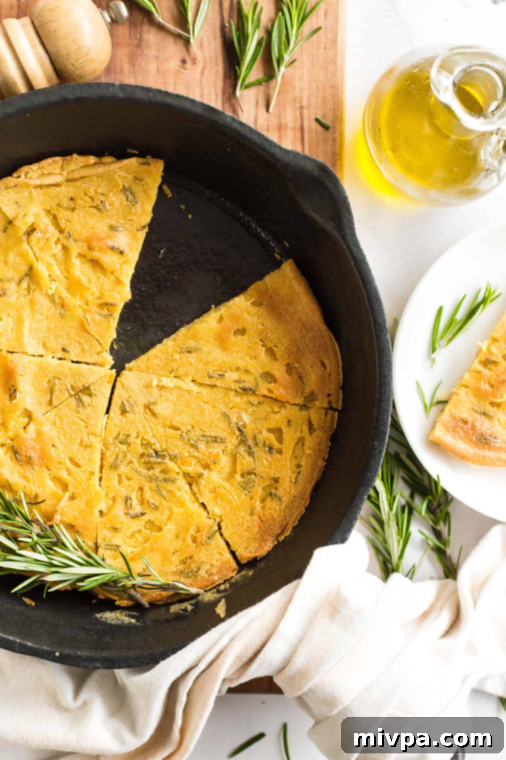 Easy Farinata Recipe - Chickpea Flatbread (Gluten-Free, Vegan) A cast iron skillet filled with golden, sliced chickpea farinata, adorned with fresh rosemary leaves.
