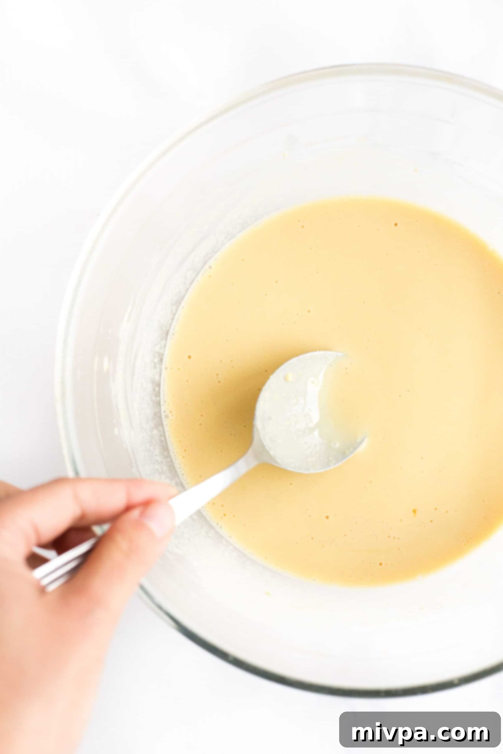 Easy Farinata Recipe - Chickpea Flatbread (Gluten-Free, Vegan) A spoon gently removing foam from the surface of the chickpea batter in a glass bowl.