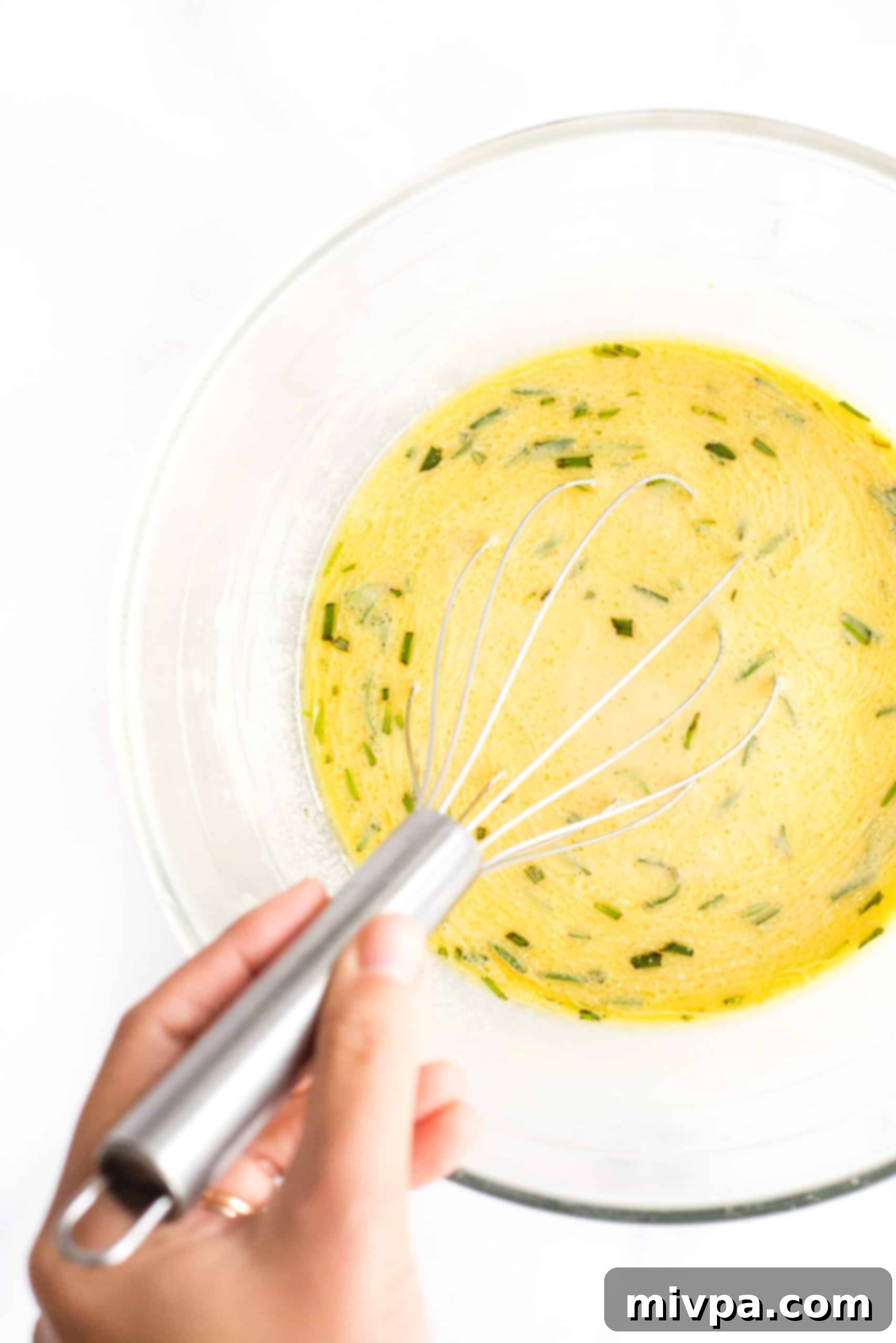 Easy Farinata Recipe - Chickpea Flatbread (Gluten-Free, Vegan) Whisking olive oil and fresh rosemary into the yellow chickpea batter in a glass bowl.