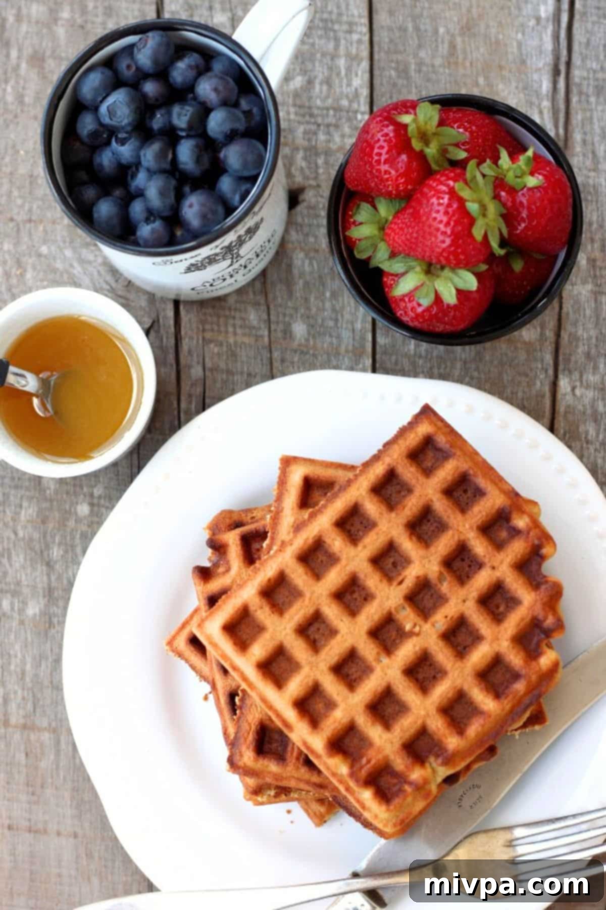 Top down view of a plate of oat waffles with a bowl of fresh mixed berries.