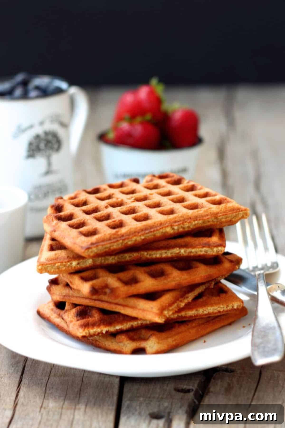 Close-up of a perfectly cooked oat waffle, garnished with berries and maple syrup.