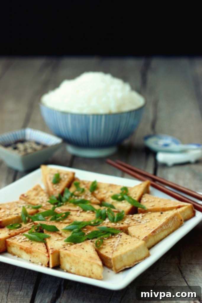 Close-up of freshly pan-fried tofu, perfectly golden and crispy, garnished with sesame seeds and spring onions