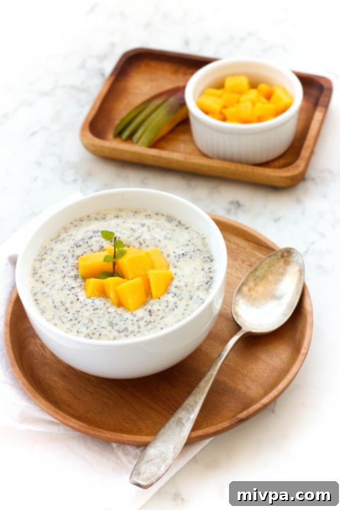 Mango Chia Pudding (Gluten-Free, Vegan) A bowl of mango chia pudding topped with fresh mangoes and mint, served on a rustic wooden surface.