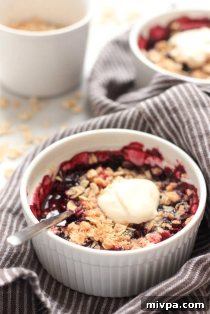 Gluten-free Berry Crisp (Dairy-Free, Vegan) Close-up of a single ramekin filled with a vibrant gluten-free mixed berry crisp, showing the bubbling fruit and golden oat topping.