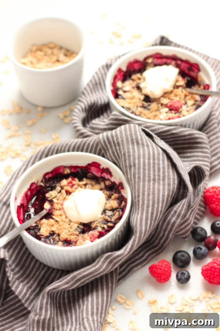 Gluten-free Berry Crisp (Dairy-Free, Vegan) Gluten-free mixed berry crisp served in a ramekin with a scoop of vanilla dairy-free ice cream on top, ready to be enjoyed.