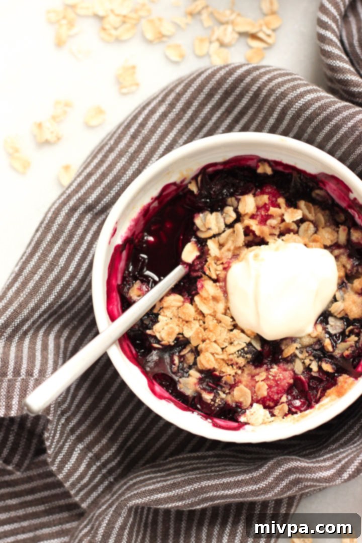 Gluten-free Berry Crisp (Dairy-Free, Vegan) An up-close, enticing shot of a single ramekin filled with warm, golden-brown gluten-free mixed berry crisp, showing the textured topping and juicy fruit underneath.