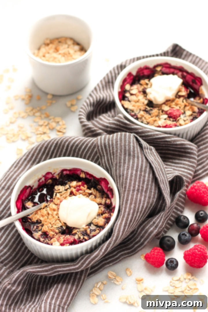 Gluten-free Berry Crisp (Dairy-Free, Vegan) A collection of bowls filled with warm berry crisp, surrounded by fresh oats and mixed berries, highlighting the rustic appeal of the dessert.