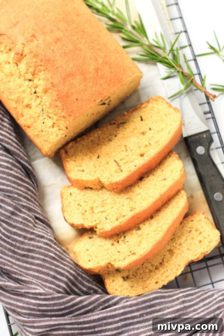 A sliced loaf of cornbread with a kitchen towel at the side.