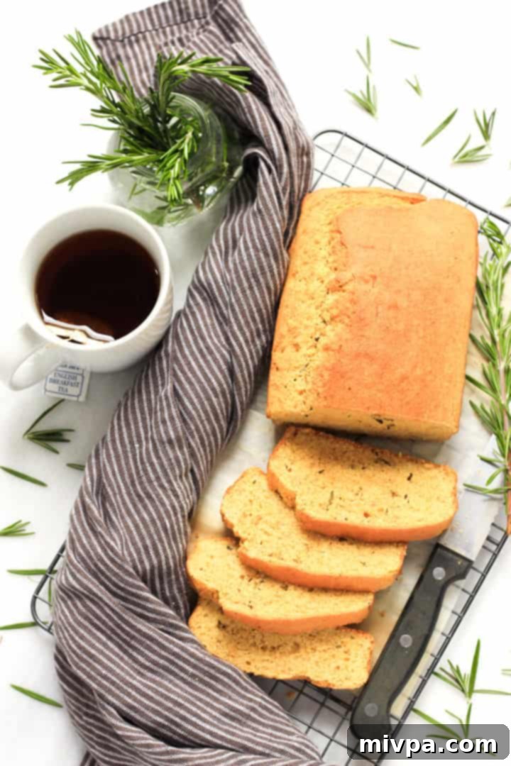 Top down view of a halfway sliced loaf of rosemary cornbread and a cup of tea by the side.