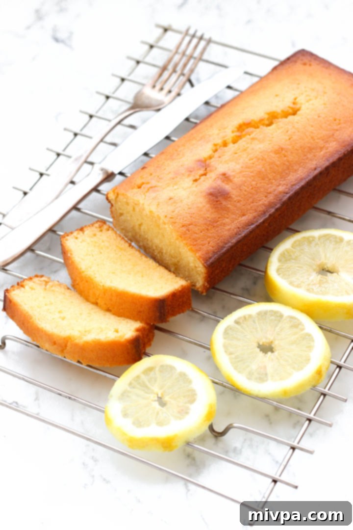 Close up shot of a sliced gluten-free lemon yogurt cake and lemon slices on cooling rack.