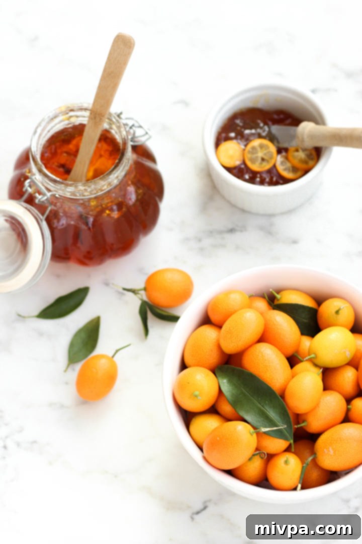 Easy Kumquat Marmalade Recipe (Gluten-Free, Vegan, Pectin-Free) A bowl of fresh kumquats and a jar of kumquat jam on a marble board. The vibrant orange kumquats contrast with the rich, golden hue of the homemade marmalade, inviting a taste.