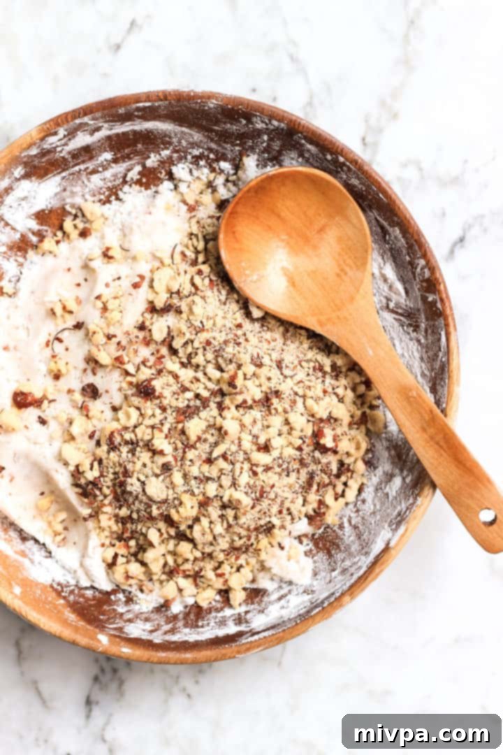 Close-up of hazelnut cookie dough in a wooden bowl, studded with chopped hazelnuts.