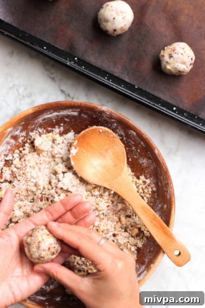 Cookie dough in a bowl and neatly rolled cookie dough balls on a silpat-lined baking sheet.