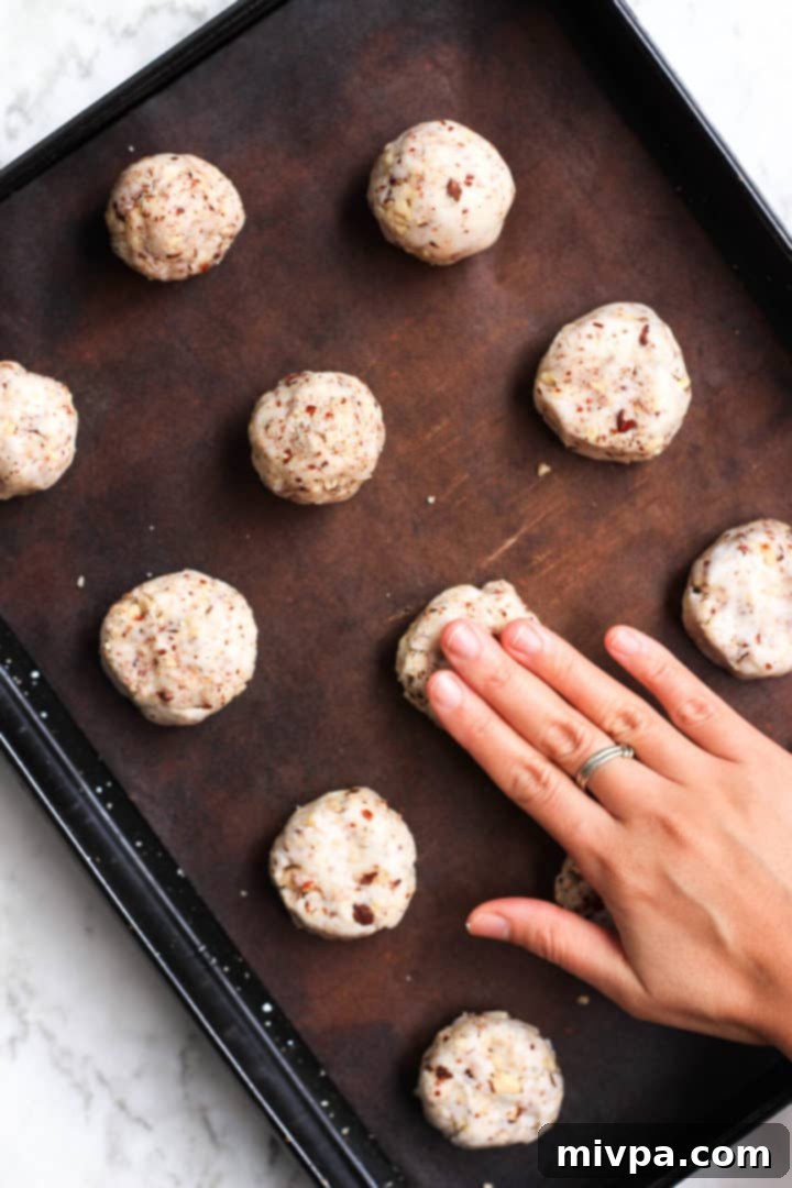 A hand gently flattening a cookie dough ball on a silpat baking mat.