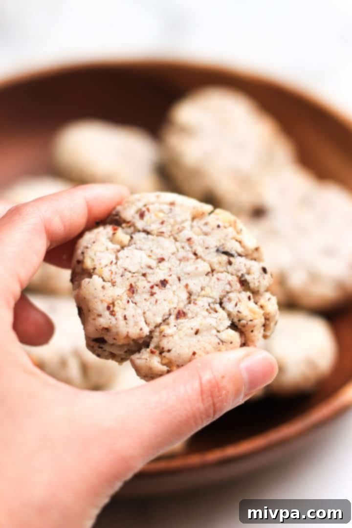 A hand delicately holding a single crispy gluten-free hazelnut cookie, showcasing its perfect texture.