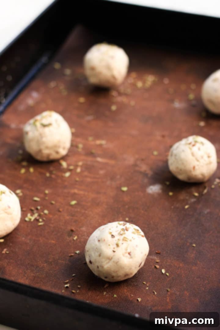 Raw dough balls for gluten-free bread rolls, sprinkled with oregano, ready for baking on parchment paper.