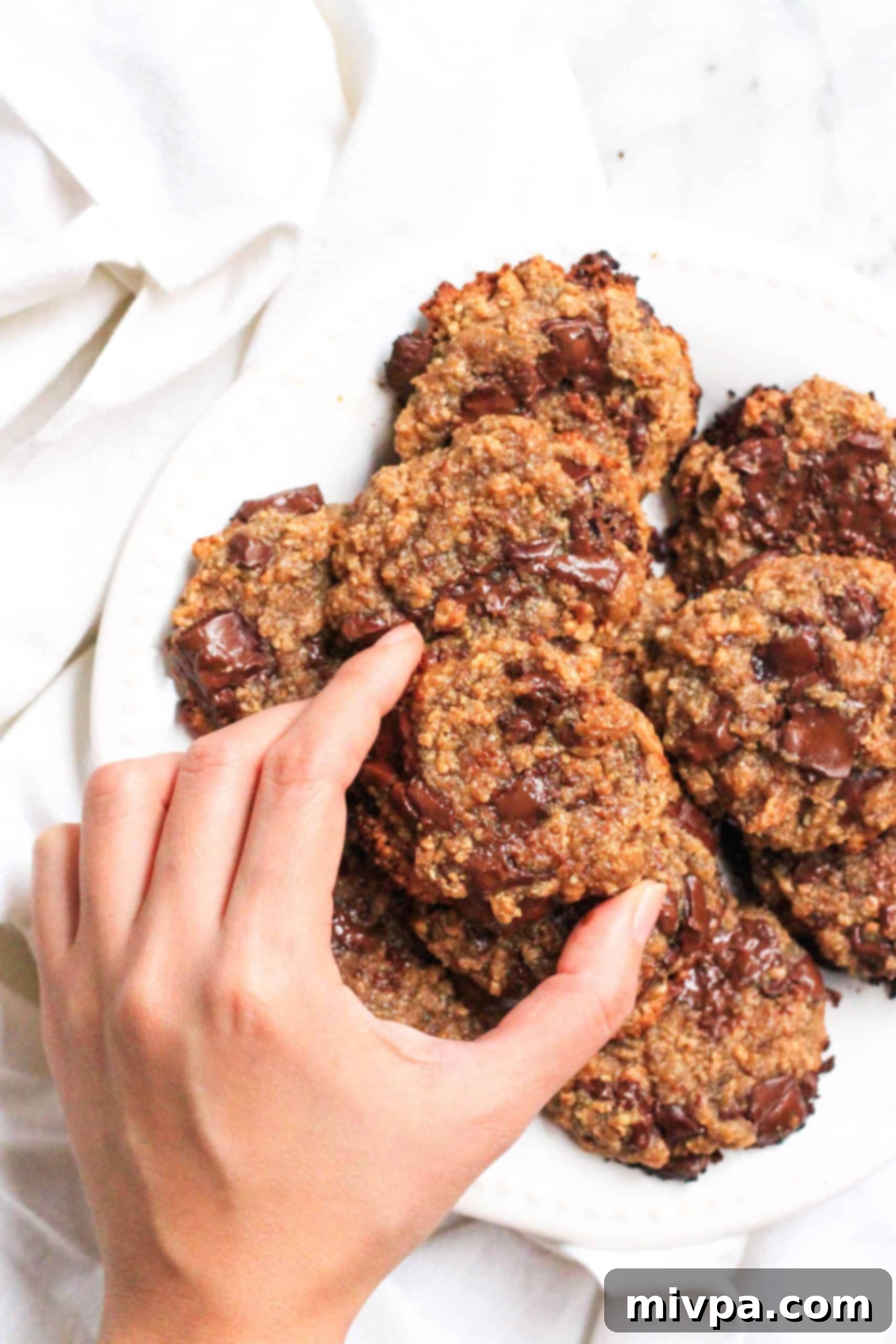 Easy Cashew Butter Cookies (Gluten-Free, Dairy-Free, Vegan) Reaching for a cookie from a plate full of cashew butter cookies.