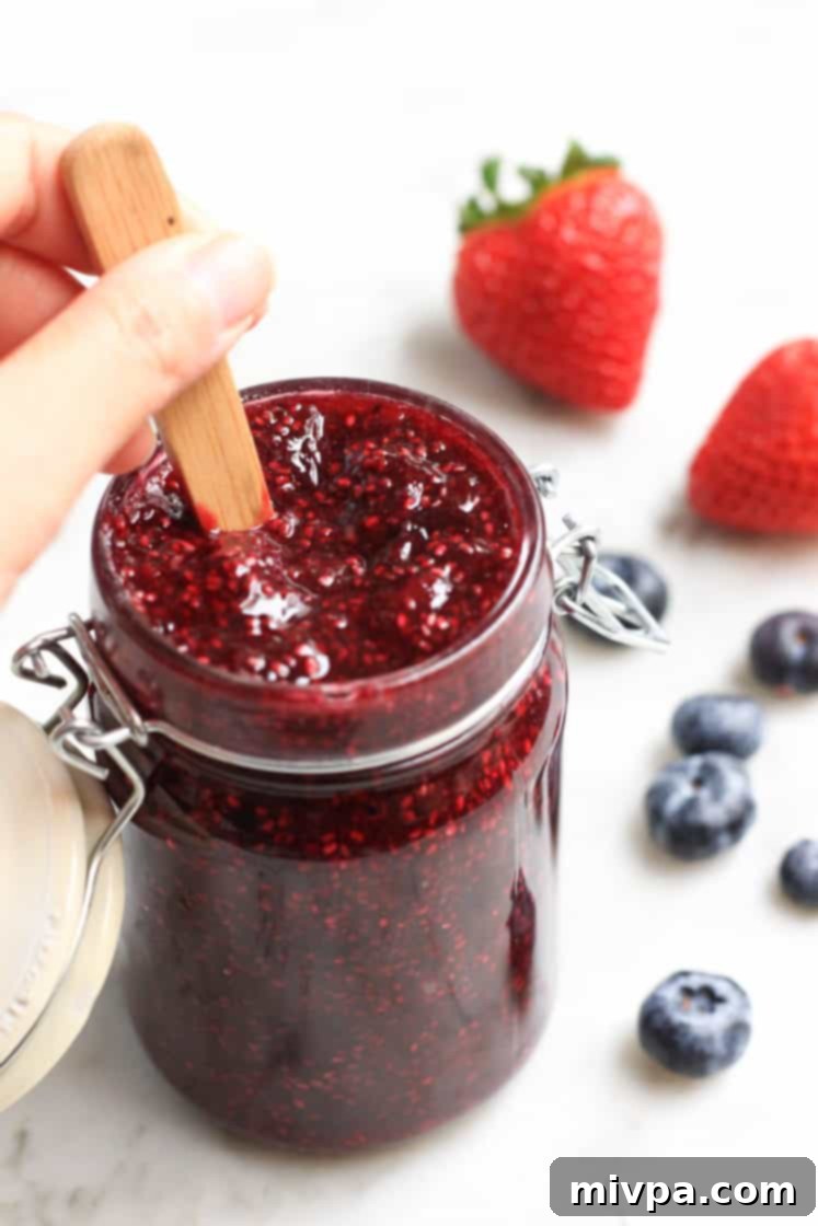 Mixed Berry Chia Seed Jam (Gluten-Free, Vegan) Hand mixing berry chia seed jam in a jar with a spoon.