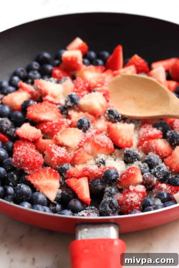 Mixed Berry Chia Seed Jam (Gluten-Free, Vegan) Using a wooden spoon to gently mix fresh berries and sugar in a skillet during the simmering process.