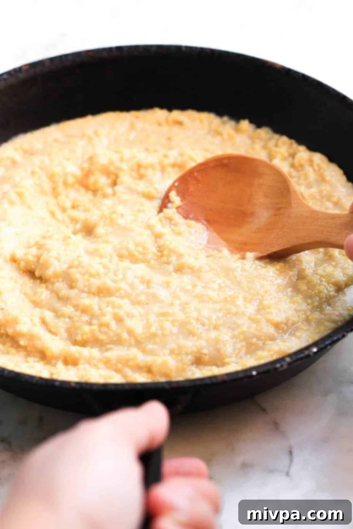 Using wooden spoon to stir millet porridge in pan.