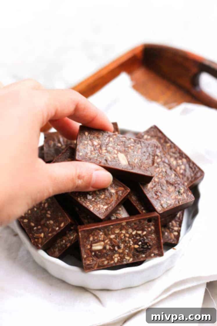 Easy Homemade Chocolate (Gluten-free, Vegan) Hand picking up a piece of homemade raisin and seed chocolate.