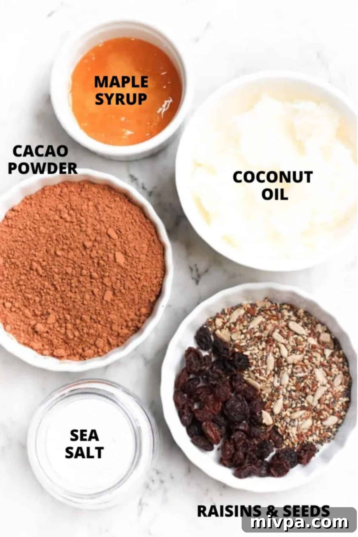 Easy Homemade Chocolate (Gluten-free, Vegan) Labeled ingredients for homemade chocolate on marble board including coconut oil, cocoa powder, maple syrup, raisins, and seeds.