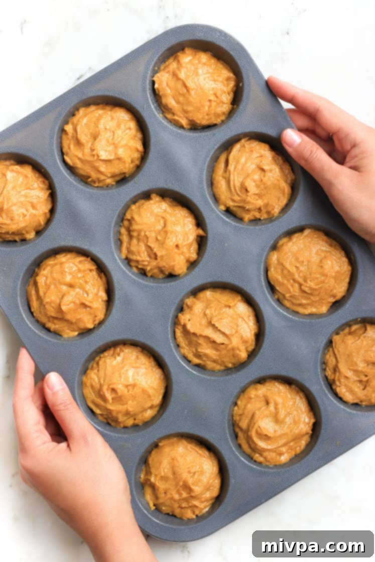 Hands carefully holding a silicon muffin mold, with each cavity perfectly filled with pumpkin muffin batter.